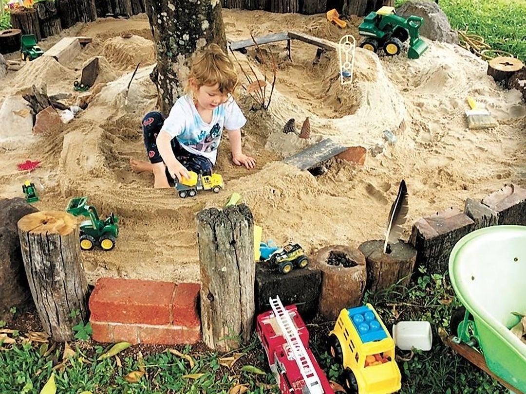 Barn der leger i den kæmpe sandkasse omkring træet